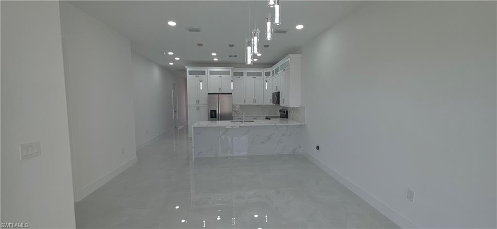 Modern kitchen featuring white cabinetry, a stainless steel refrigerator, and a light-toned countertop with a waterfall edge