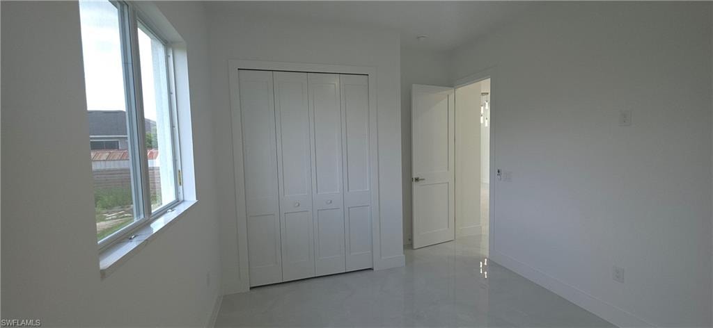 Bright interior room featuring a multi-pane window, bi-fold closet doors, a paneled door, and reflective flooring