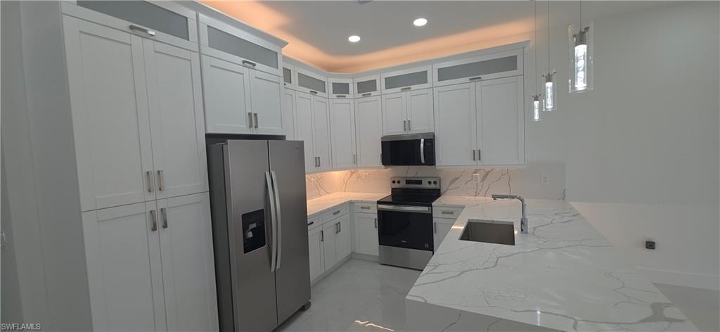 Kitchen featuring white shaker cabinetry, an integrated stainless steel sink, under-cabinet lighting, and a countertop with subtle veining