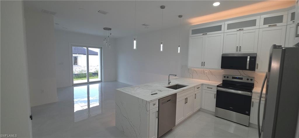 Modern kitchen featuring white cabinetry, quartz countertops, a stainless steel appliance suite, and contemporary pendant lighting