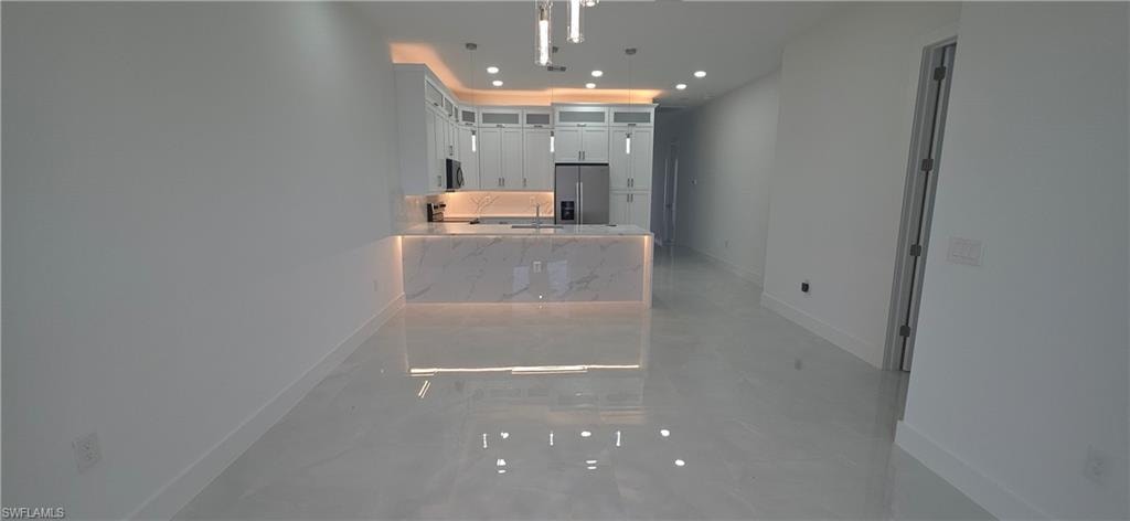 Open-concept kitchen and living area featuring sleek white cabinetry, a waterfall-edge island with integrated lighting, stainless steel appliances, and glossy tile flooring throughout