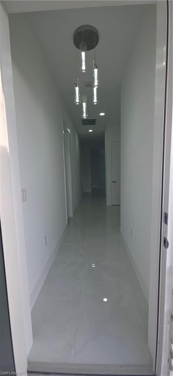 Long hallway featuring a contemporary multi-pendant light fixture, recessed lighting, white walls, white baseboards, and light-colored tile flooring