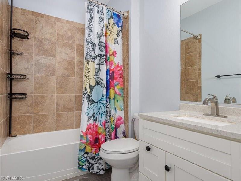Bathroom featuring a white tub, natural-toned tile surround, and a white vanity with a light speckled countertop