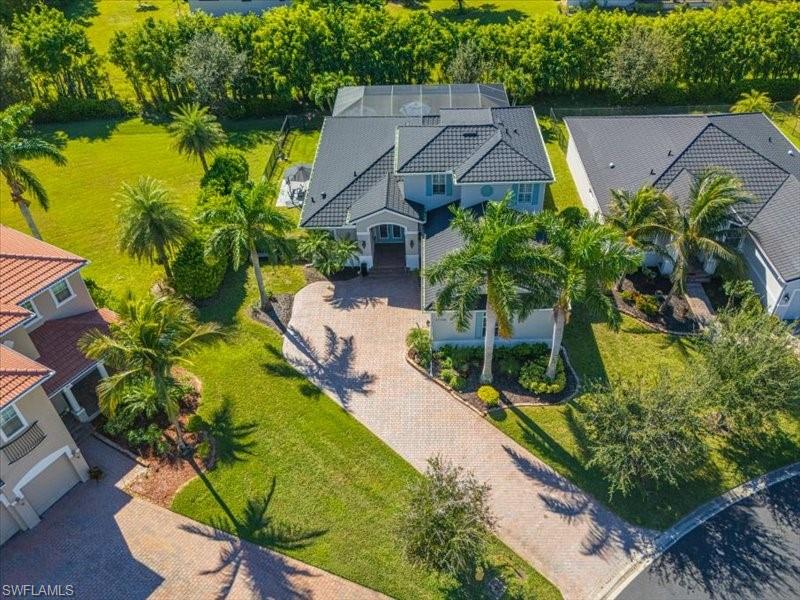 Expansive residential property featuring a large paver driveway, mature palm trees, and manicured lawns