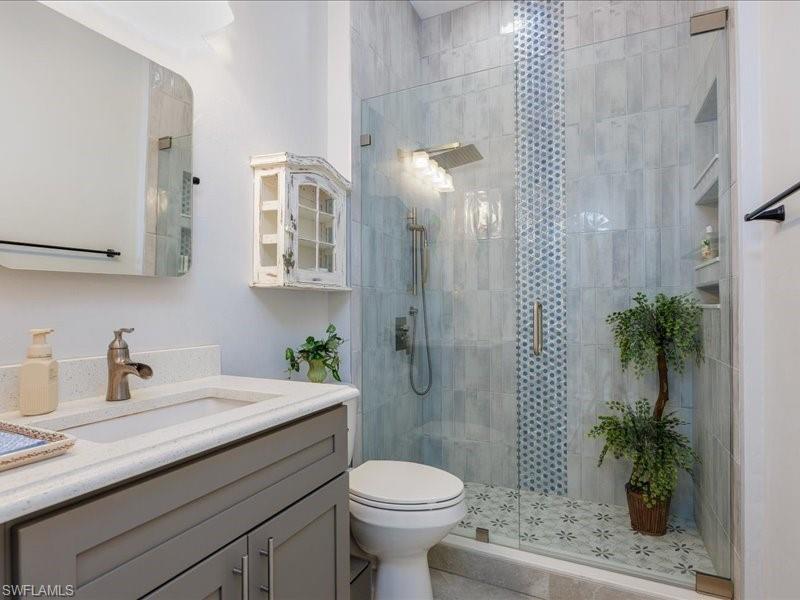 Modern bathroom featuring a glass-enclosed shower with contrasting tile inlay, built-in shower niches, a rainfall showerhead, and a vanity with an integrated sink and quartz countertop