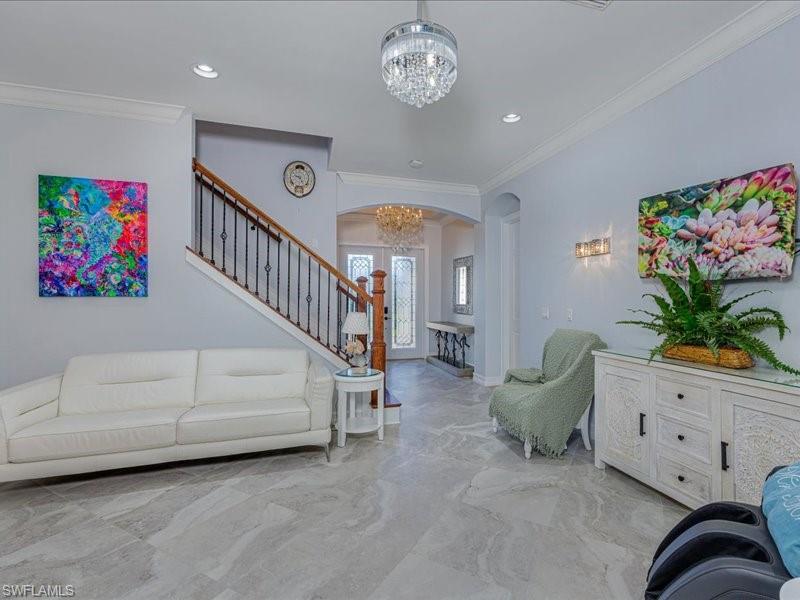 Spacious interior featuring large-format tile flooring, crown molding, recessed lighting, a staircase with wood handrails and wrought iron balusters, and a decorative chandelier