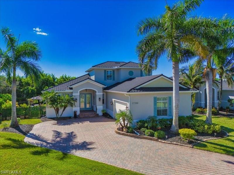 Stucco exterior with a tiled roof, featuring a paver driveway, mature palm trees, and established landscaping