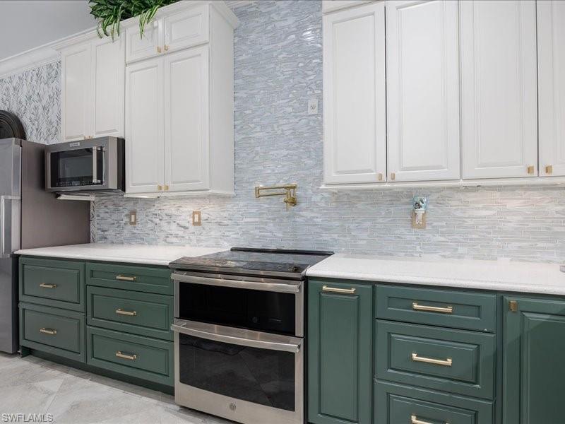 Kitchen featuring two-tone cabinetry with white upper cabinets and green lower cabinets, stainless steel appliances, white countertops, and a full-height tile backsplash with a linear pattern