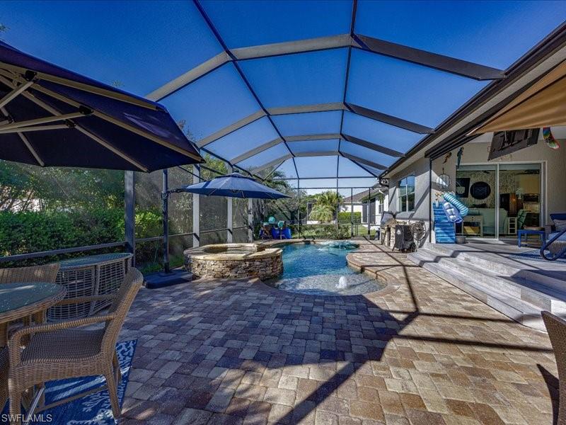 Screened outdoor living area featuring a paver patio, integrated spa, and swimming pool with water features