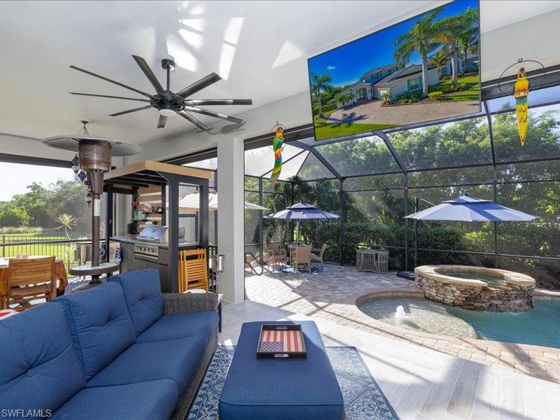 Screened lanai featuring wood-finish flooring, a built-in outdoor kitchen, a large ceiling fan, and a stone-accented spa with water feature