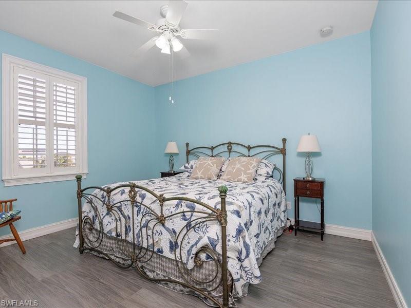 Window with plantation shutters, wood-finish flooring, white ceiling fan with integrated lighting, and white baseboards