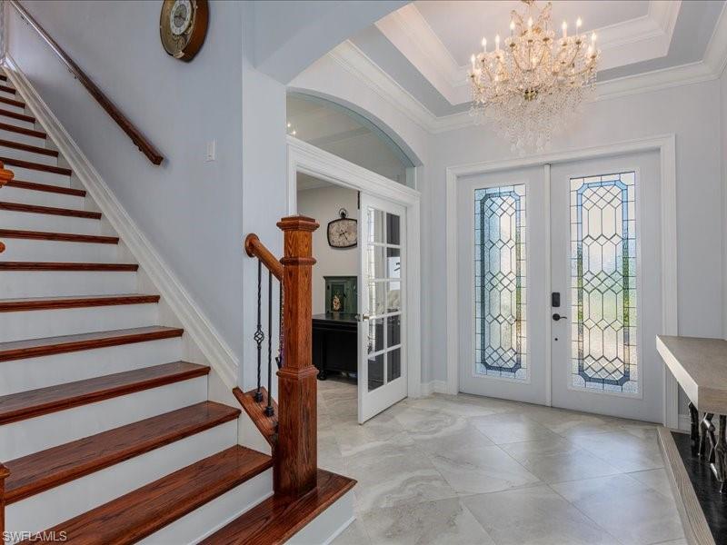 Grand foyer featuring double entry doors with decorative glass panels, a coffered ceiling with a tiered crystal chandelier, and large format tile flooring