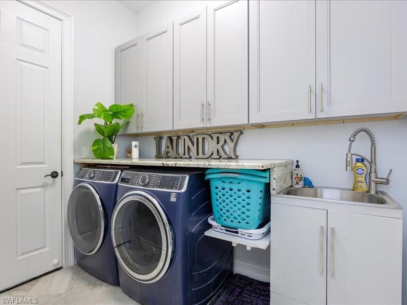 Dedicated laundry area featuring upper and lower cabinetry, stone-finish countertops, stainless steel utility sink, and wall-mounted faucet