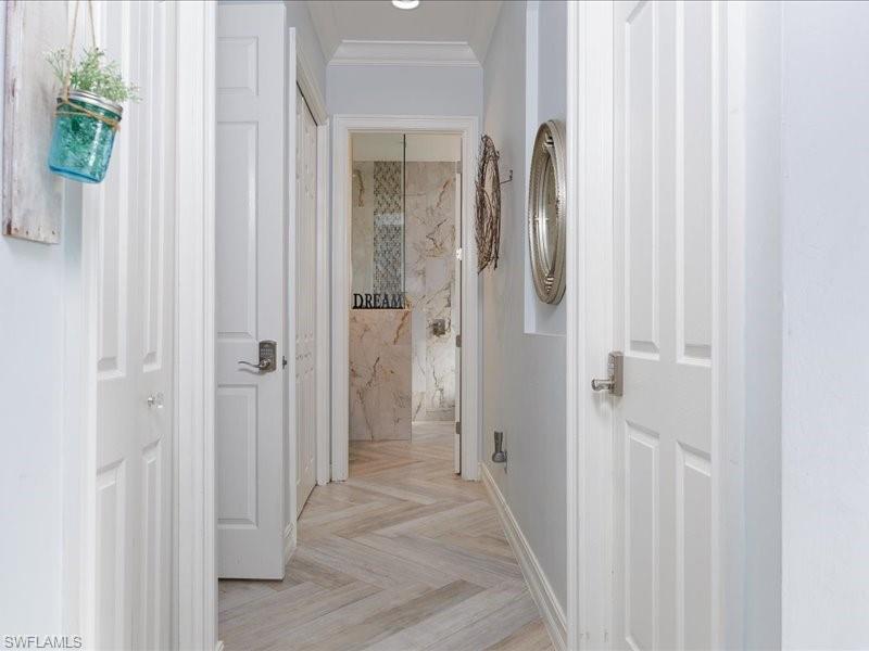 Hallway featuring wood-finish flooring in a herringbone pattern, white paneled doors with brushed nickel hardware, and light-toned wall paint