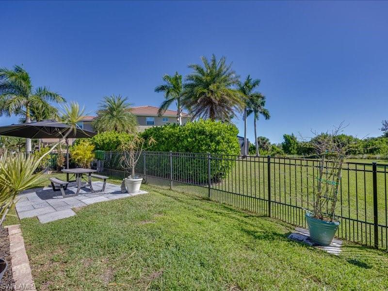 Expansive grassy yard featuring a black metal perimeter fence and a stone paver patio