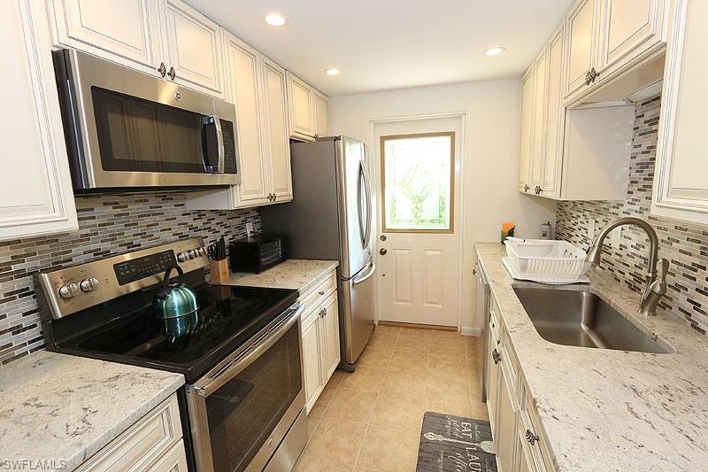 Kitchen with stainless steel appliances, sink, tasteful backsplash, and light stone counters