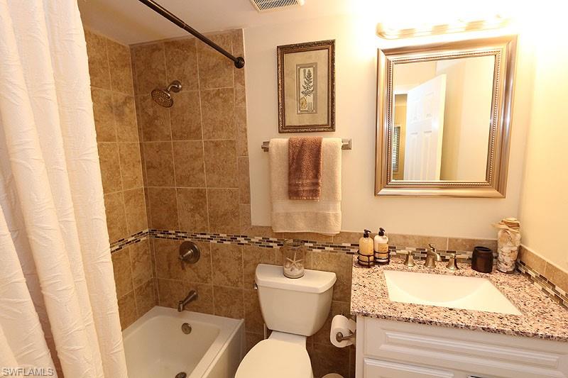 Full bathroom featuring tile walls, large vanity, toilet, and shower / bath combo with shower curtain