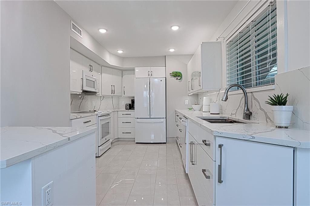 Kitchen featuring tasteful backsplash, white appliances, light stone counters, sink, and white cabinets