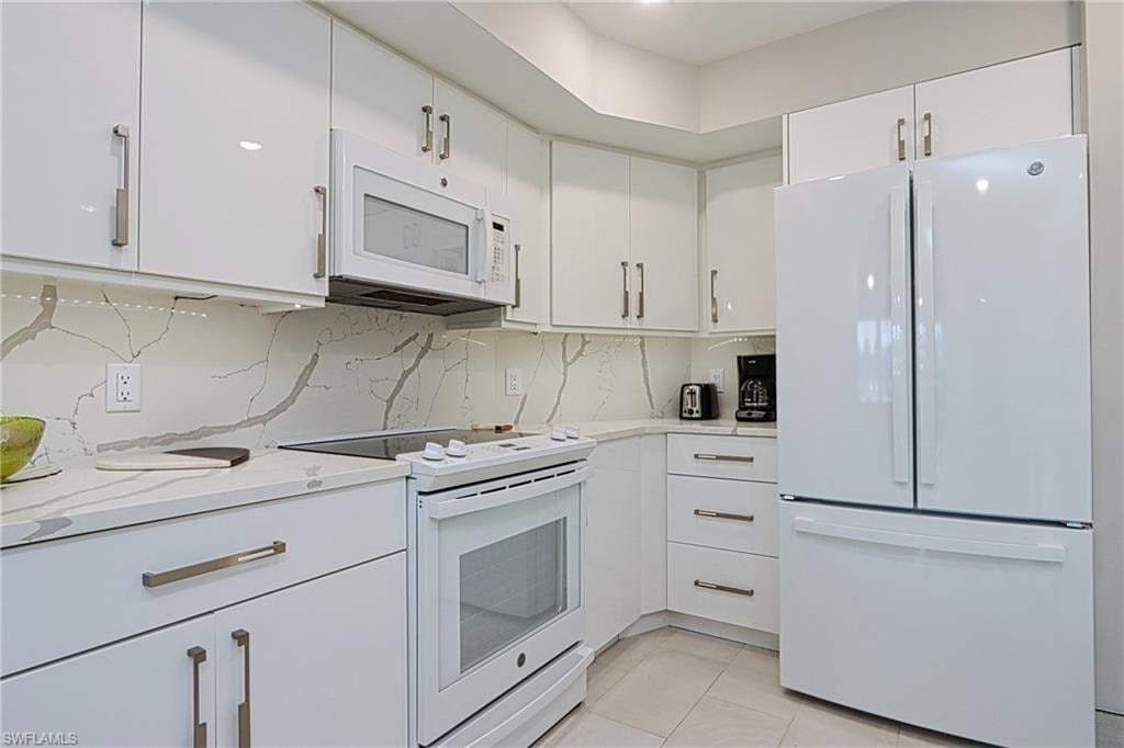 Kitchen with light stone counters, tasteful backsplash, white cabinetry, white appliances, and light tile floors