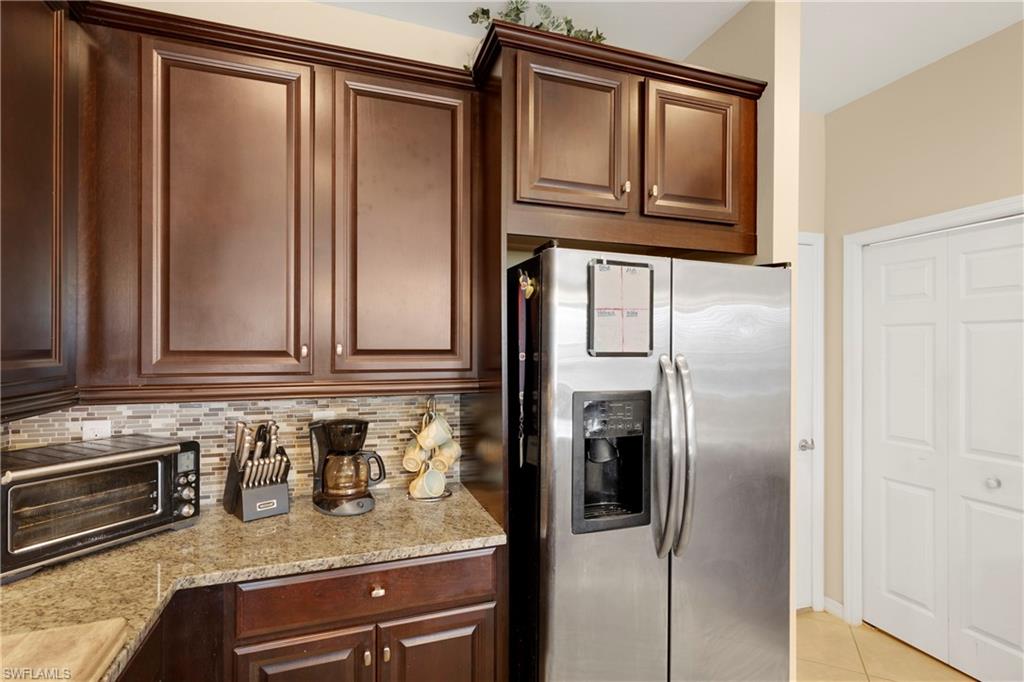 Kitchen featuring stainless steel fridge, decorative backsplash, light tile patterned floors, dark brown cabinetry, and light stone counters