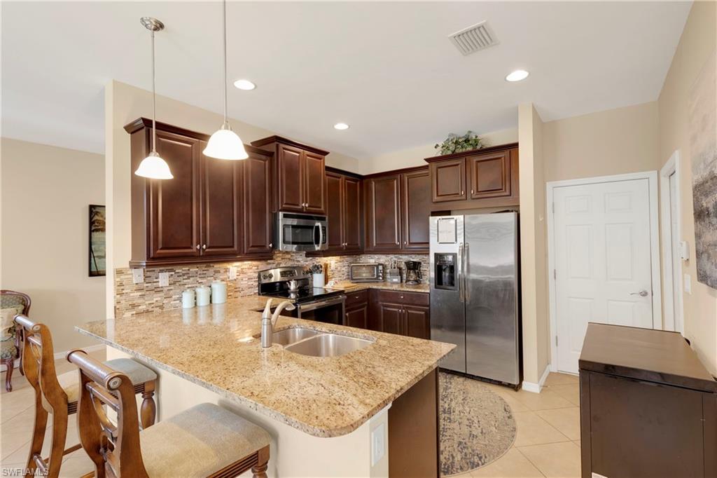 Kitchen featuring appliances with stainless steel finishes, backsplash, a kitchen bar, hanging light fixtures, and kitchen peninsula