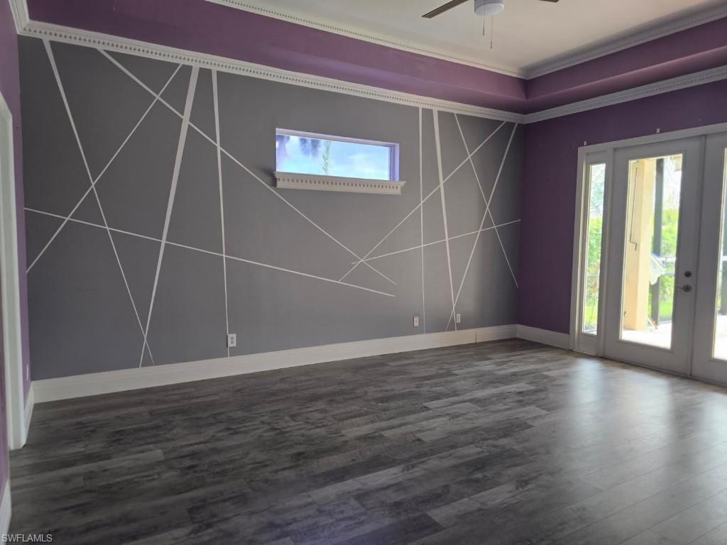 Spacious room featuring wood-finish flooring, a tray ceiling, crown molding, and direct access to outdoor space via glass-paneled French doors