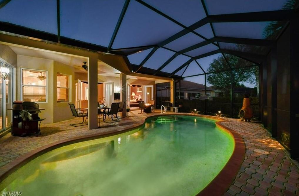 Screened-in pool area featuring a curved swimming pool with brick paver decking and a surrounding water feature