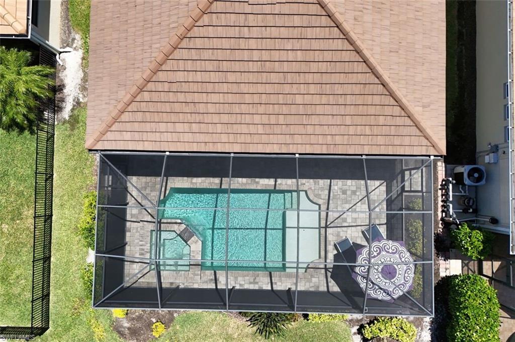 Screened pool enclosure featuring a rectangular swimming pool with integrated spa, paver decking, and a terracotta tile roofline