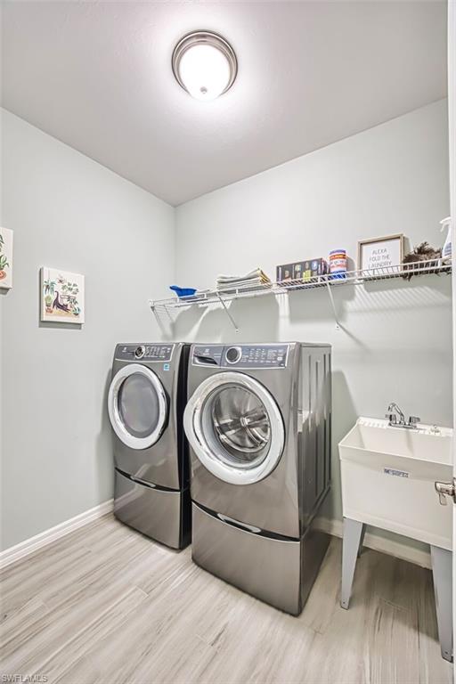 Dedicated laundry area featuring wood-finish flooring, a utility sink, and wall-mounted shelving