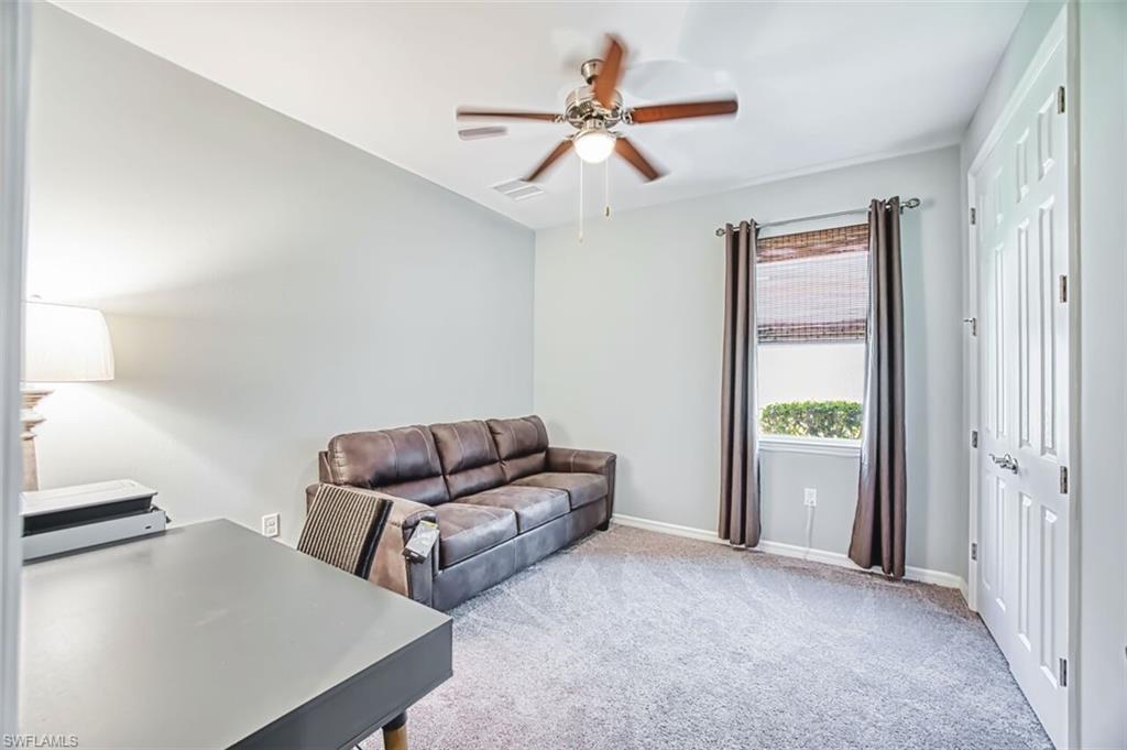 Room featuring light gray wall paint, a ceiling fan with integrated lighting, a window with a woven shade and dark fabric drapes, and gray carpeting