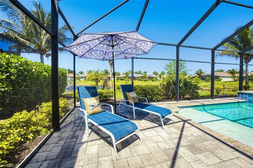 Screened pool enclosure featuring a paver deck, clear blue water, and lush perimeter landscaping