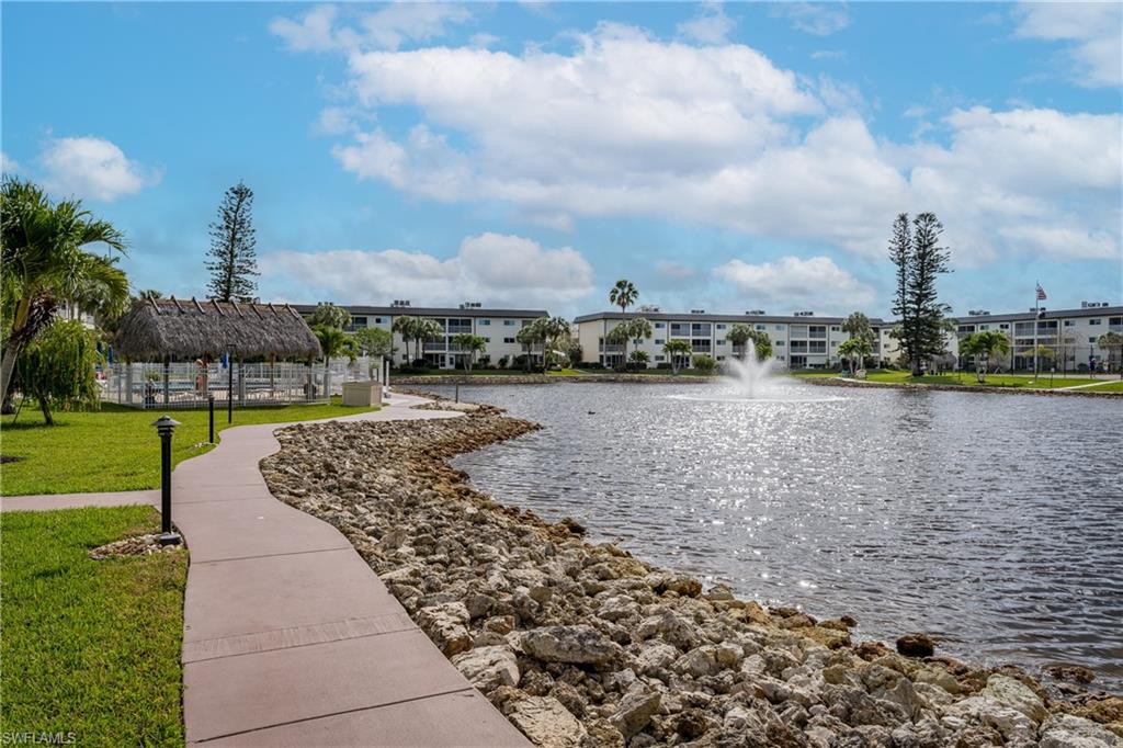 Waterfront property featuring a fountain, rock-lined shore, and manicured landscaping