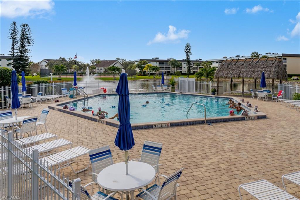Outdoor swimming pool with a surrounding paver deck, perimeter fencing, and a thatched-roof cabana
