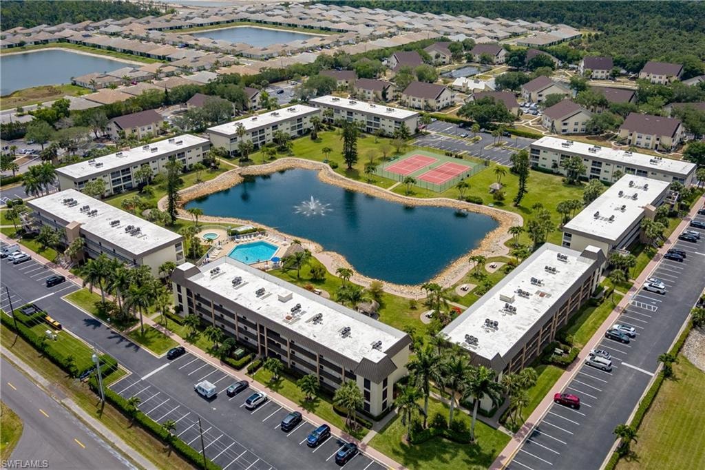 Aerial perspective showcasing a community with multiple residential buildings, a central pond with a fountain, a swimming pool, and tennis courts