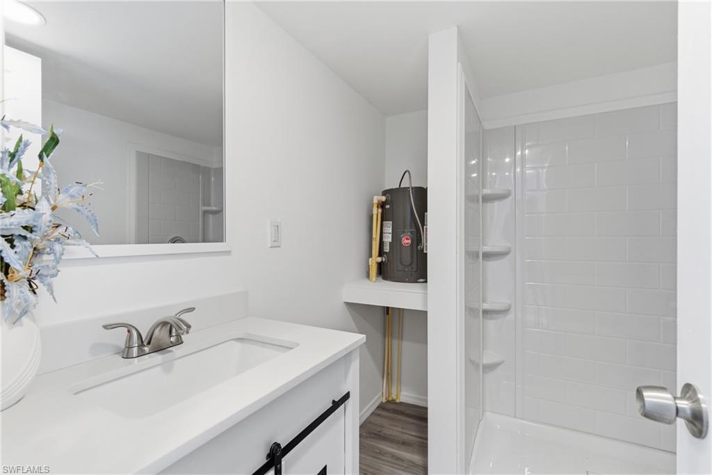 Full bath with vanity, electric water heater, a shower stall, and light wood-style floors