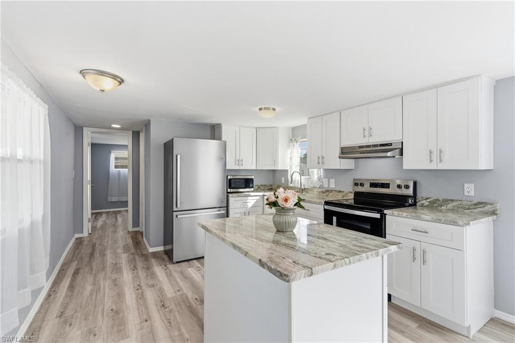 Kitchen with appliances with stainless steel finishes, white cabinets, a kitchen island, light stone countertops, and under cabinet range hood