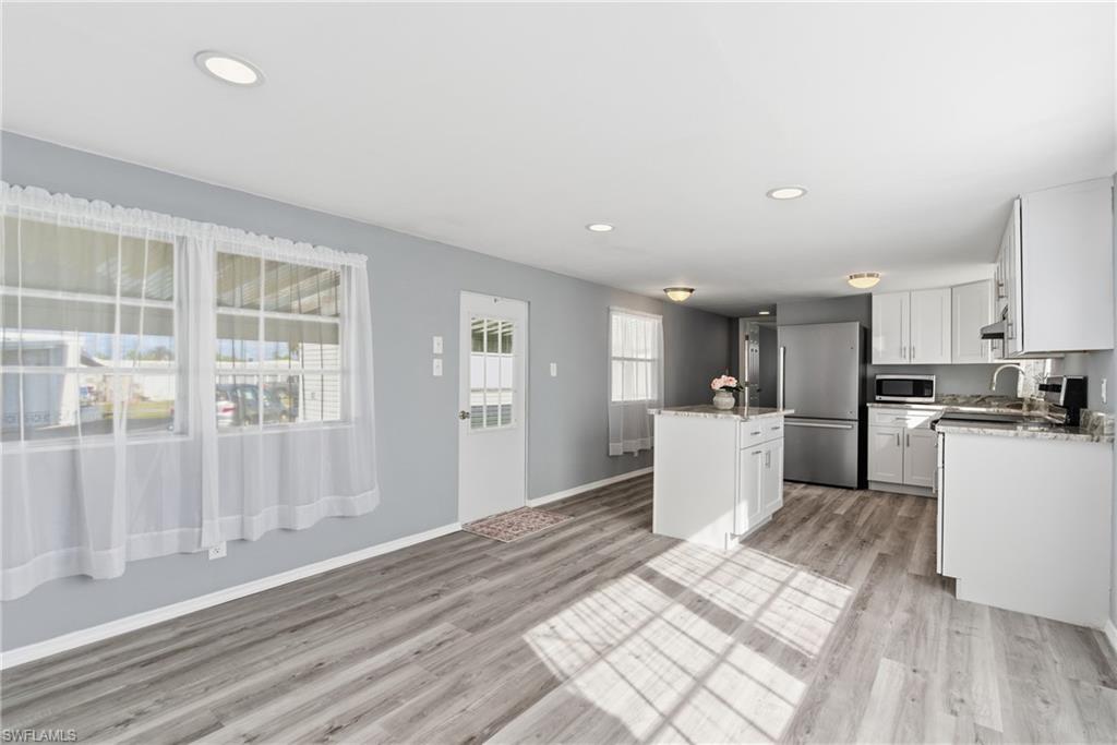 Open concept Livingroom and Kitchen with white cabinets, a kitchen island, appliances with stainless steel finishes, recessed lighting, and light stone countertops
