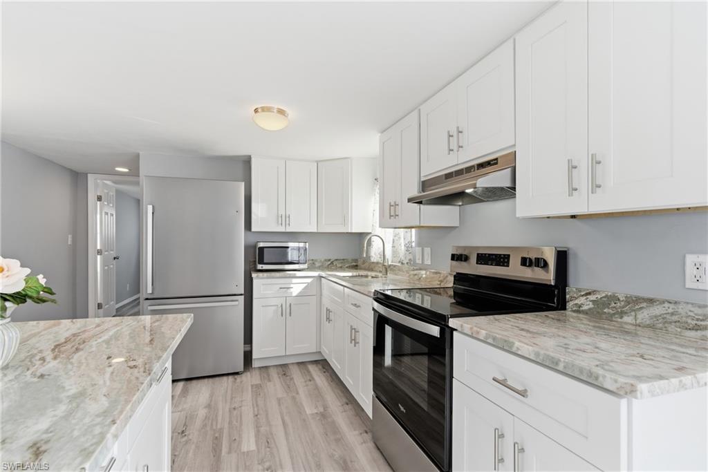 Kitchen featuring stainless steel appliances, white cabinets, under cabinet range hood, and light wood finished floors