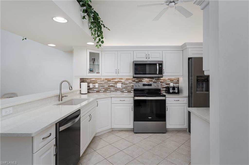 Bright kitchen featuring white cabinetry, light-toned countertops, a mosaic tile backsplash, stainless steel appliances, and diagonal tile flooring