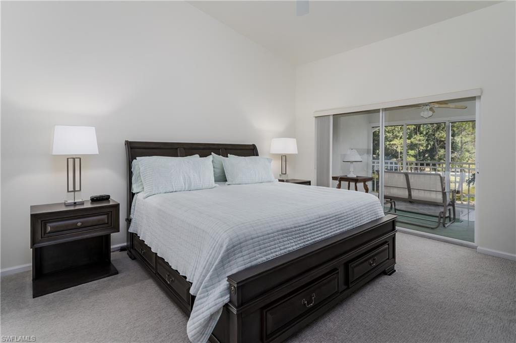 Bedroom featuring vaulted ceilings, plush carpet flooring, and direct access to an enclosed porch with tree-lined scenery