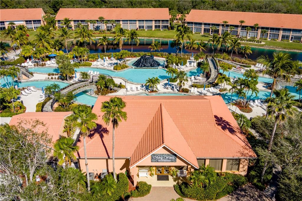 Expansive property featuring a large swimming pool complex, multiple buildings with terracotta-style roofs, lush tropical landscaping with numerous palm trees, a winding waterway, and pedestrian bridges