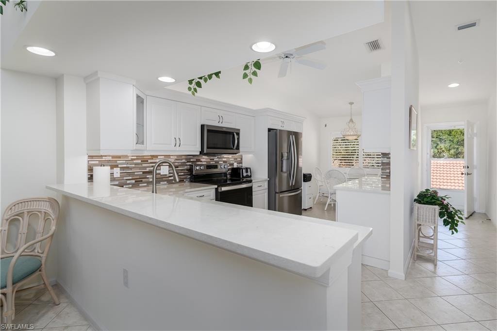 Well-appointed kitchen featuring white cabinetry, stainless steel appliances, a multi-tone tile backsplash, and a breakfast bar with a light-toned countertop