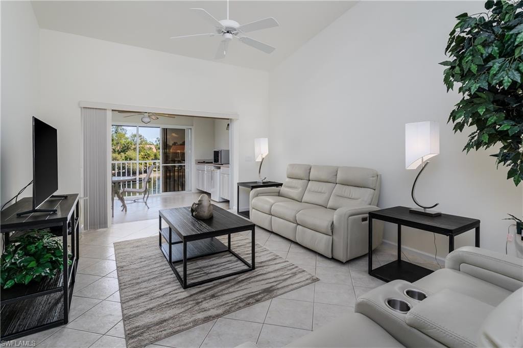 Vaulted ceilings enhance this living area featuring tile flooring, a ceiling fan, and sliding glass doors opening to a balcony with water views