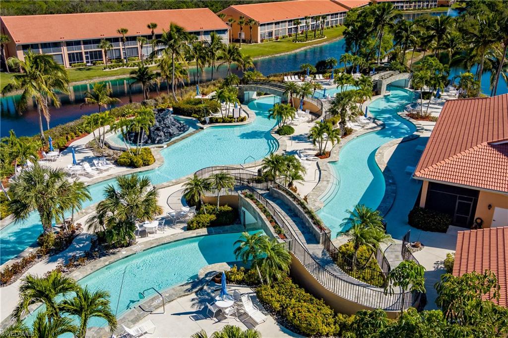 Expansive resort-style swimming pool featuring a lazy river, multiple bridges, a rock grotto, abundant lounge seating, and surrounding tropical landscaping