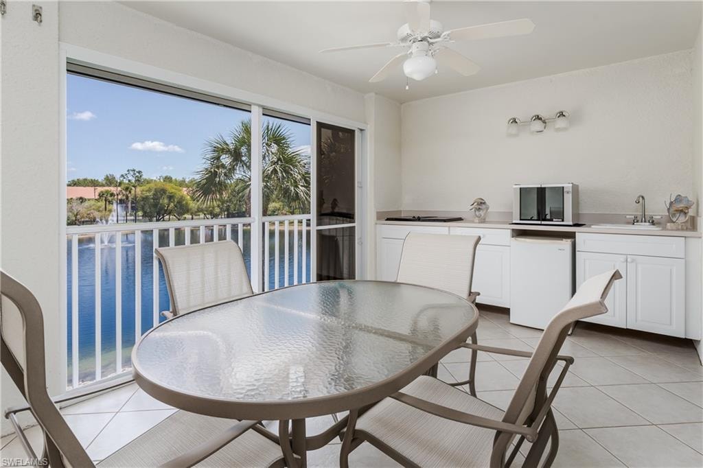 Screened patio featuring a water view with palm trees, built-in cabinetry, an integrated sink, a ceiling fan, and tiled flooring
