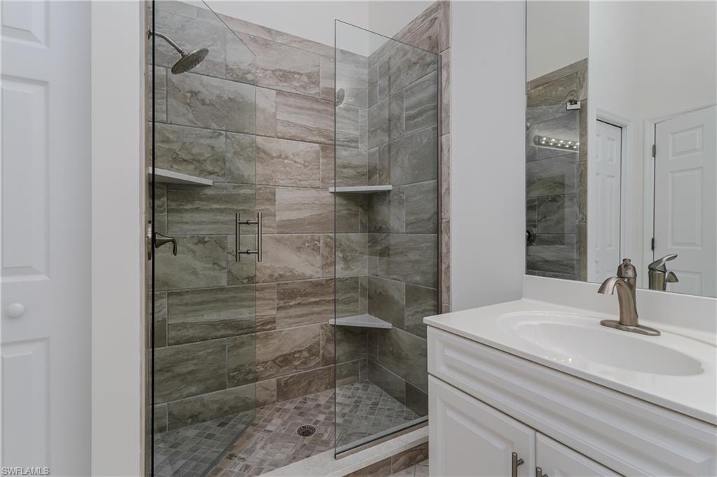 Tiled shower enclosure with a glass door, rain showerhead, and integrated corner shelving