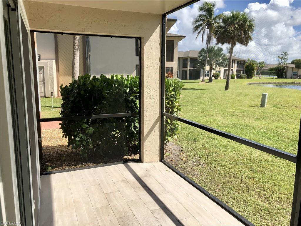 Screened patio with wood-finish flooring, overlooking a green expanse, mature palm trees, and a tranquil pond