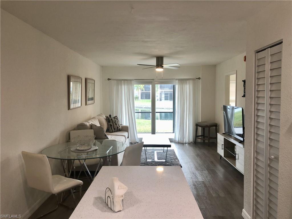 Living area featuring wood-finish flooring, a ceiling fan with integrated lighting, and a glass sliding door leading to an exterior space with water beyond