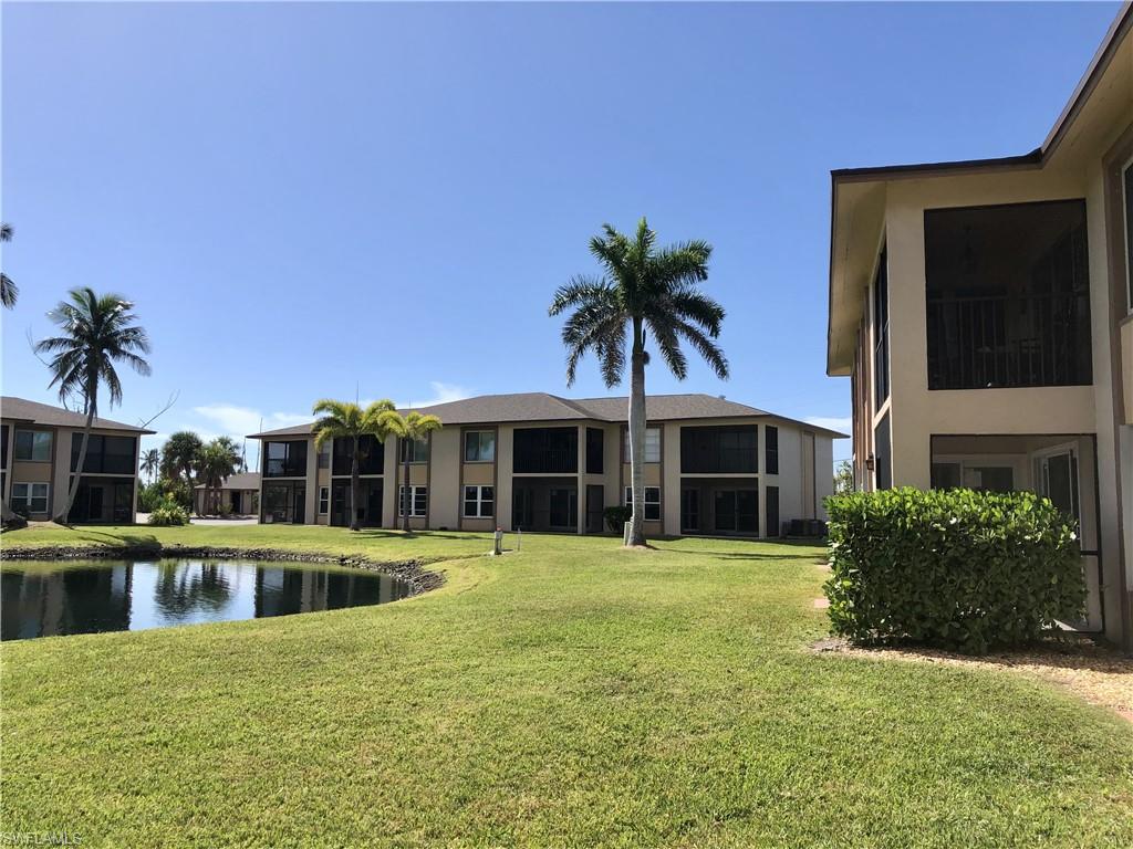 Lush green lawn with a curved pond, bordered by mature palm trees and low-rise residential buildings featuring screened lanais