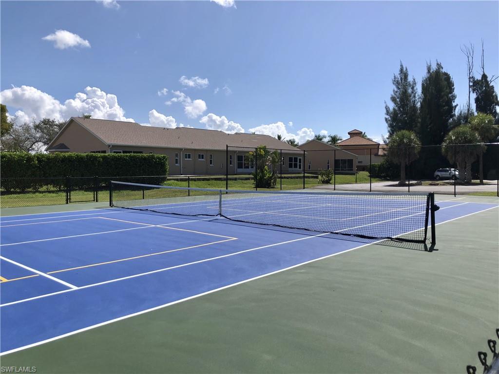 Sport court featuring a blue playing surface and green surrounds, complete with a net and perimeter fencing